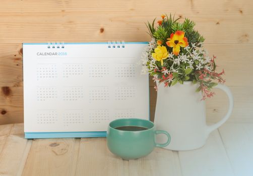 Blank calendar with cup and vase on wood table with light tone