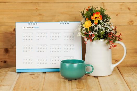 Blank calendar with cup and vase on wood table with yellow light tone

