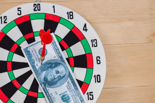 Dart arrow hitting in bullseye on dartboard with money
