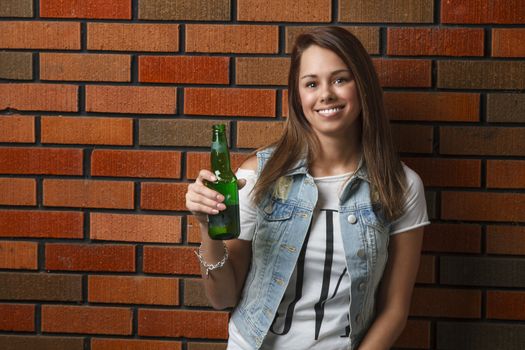 twenty something girl holding a green bottle of beer against a brick wall