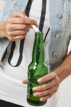 close up of a teenage girl putting a cigarette in a bottle of beer