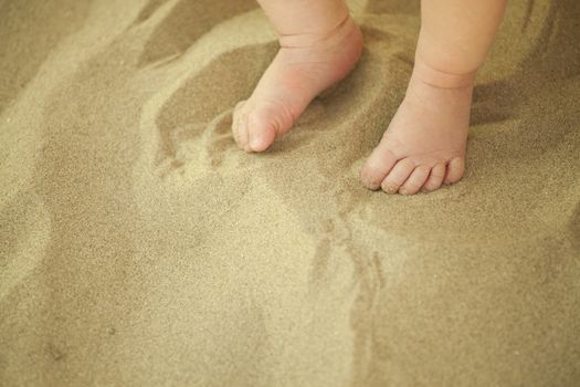 Newborn baby feet playing in the sand in summertime