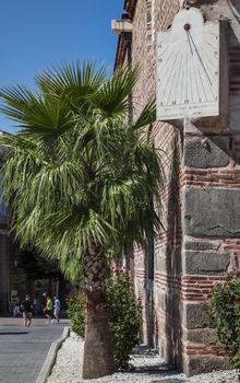 Sun clock and a palm tree on the corner of Dzhuaya, Djumaya Mosque or Cuma Camii in turkish, downtown Plovdiv on a sunny summer day.