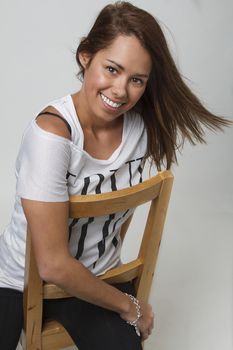 young woman in her twenties, sitting on a wood chair