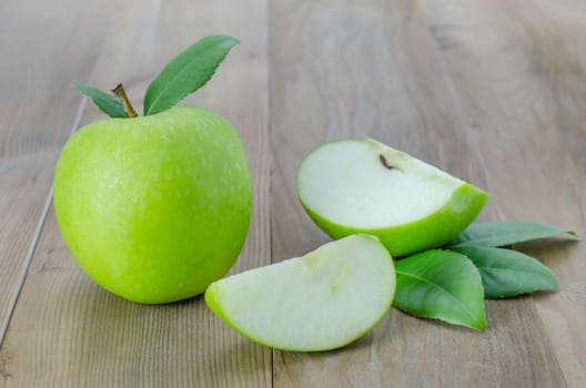 Ripe green apple with leaf and slice on a wooden background