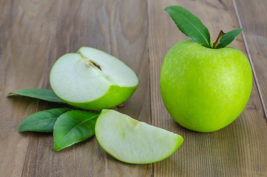 Ripe green apple with leaf and slice on a wooden background