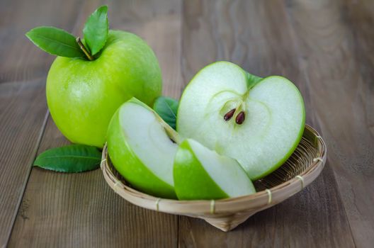 Ripe green apple with leaf and slice on a wooden background