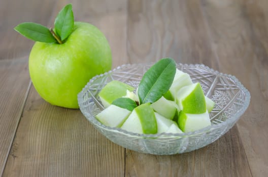 Ripe green apple with leaf and slice on a wooden background