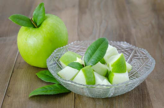 Ripe green apple with leaf and slice on a wooden background