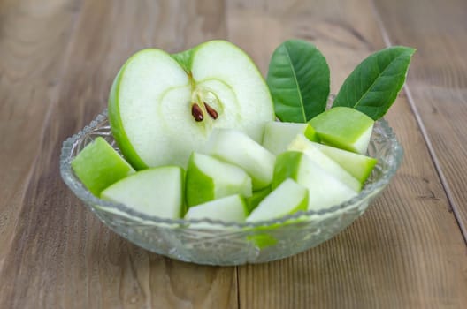 Ripe green apple with leaf and slice on a wooden background