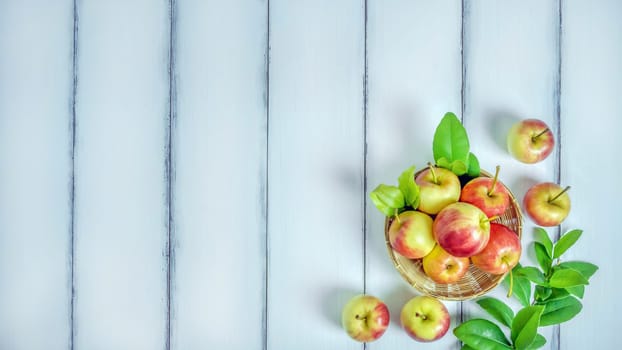 Top view red and yellow apple with leaves and  bamboo basket on  white wooden background with free space for text
