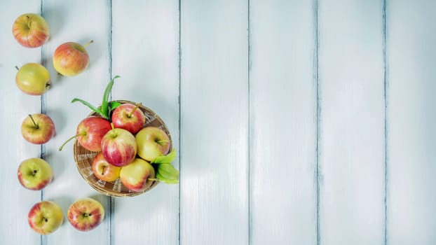 Top view red and yellow apple with leaves and  bamboo basket on  white wooden background with free space for text