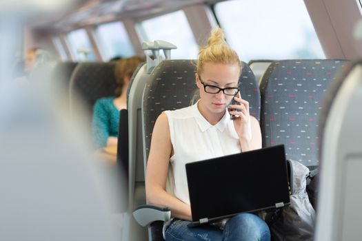 Businesswoman talking on cellphone and working on laptop while traveling by train. Business travel concept.