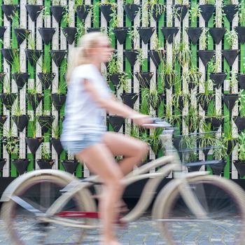 Motion blure of woman riding bycicle by green urban vertical garden wall in Ljubljana, European green capital of Europe 2016. Sustainable green city concept.