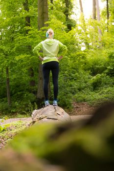 Active sporty woman standing on tree trunk while workout in nature. Wellness and healthy lifestyle concept.
