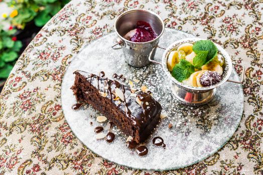 Piece of chocolate cake with fruit and ice cream is on the glass tray on the table