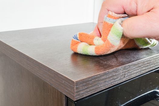 Wiping a dusty cabinet with wooden surface with a cleaning cloth.