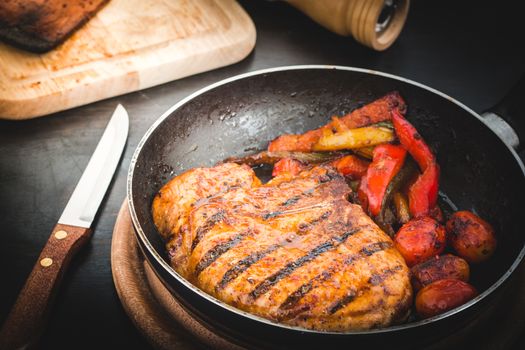 Grilled steak with tomatoes and roast vegetables on old wooden background