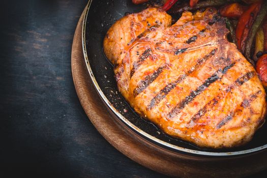 Grilled steak with tomatoes and roast vegetables on old wooden background