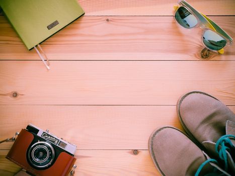 Set of travel and resort stuff. Old 35mm camera, note book, sunglasses and desert boots on wooden table. Top view, flat lay with copy space. Toned image