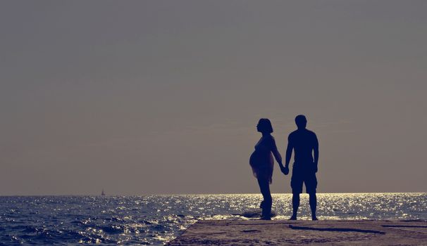 Young Family Waiting for the Miracle.  Romantic Couple on a Beach at Sunset on Background.