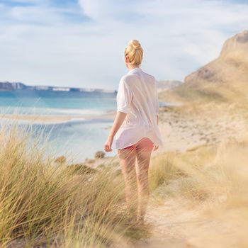 Relaxed woman in white shirt looking at distance, enjoying beautiful nature, freedom and life at serene landscape at Balos beach, Greece. Concept of vacations, freedom, happiness, joy and well being.