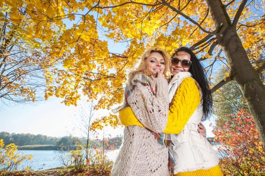 Two cheerful women in autumn park at sunny day