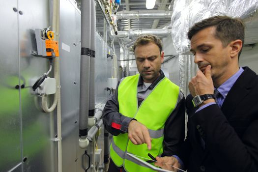 Worker and manager in electrical switchgear room of CNC plant