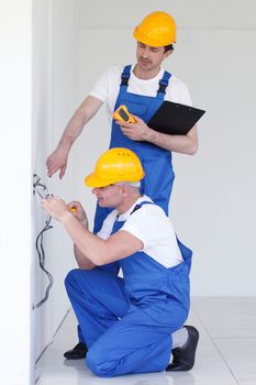 Two builders in helmets working with electricity indoors