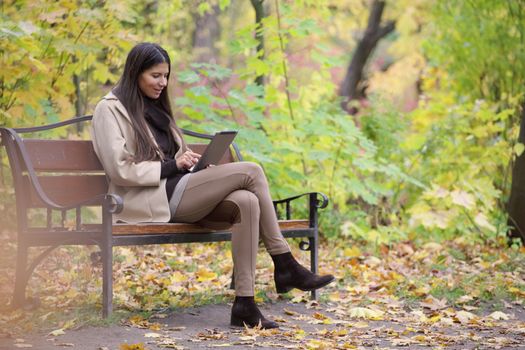 Woman using digital tablet sitting in autumn park