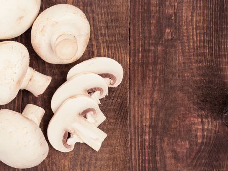 Fresh white champignon mushrooms close up on dark brown wooden background with copyspace. Flat lay or top view