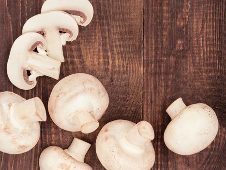 Fresh white champignon mushrooms close up on dark brown wooden background with copyspace. Flat lay or top view