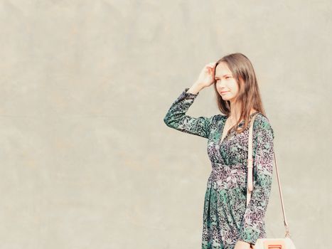 Side view of caucasian woman walking on city street in front of gray wall. Copy space