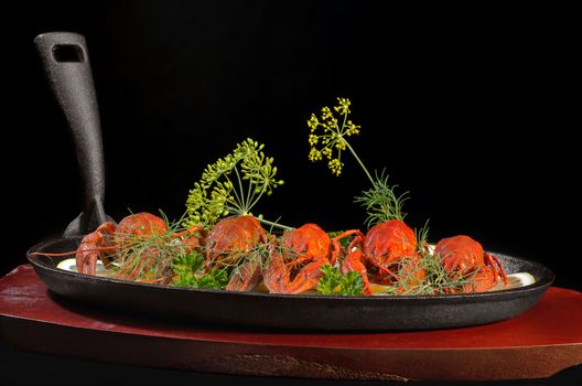 Boiled crawfish with lemon and herbs, in a pan on a wooden stand and a black background