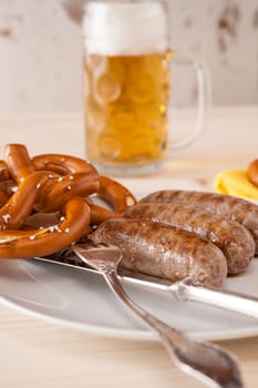 Closeup of bavarian cooked sausage and pretzel and a glass of beer on background