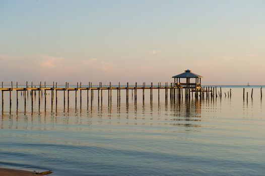 Late Evening Shot of Pier on Bay with calm water and sailboat in the distance