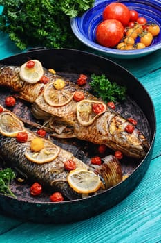 Frying pan with two baked fish in tomatoes,spices and lemon