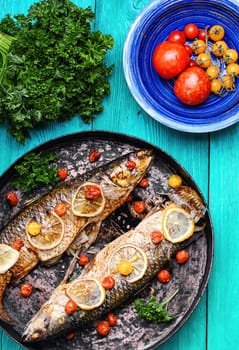 Frying pan with two baked fish in tomatoes,spices and lemon