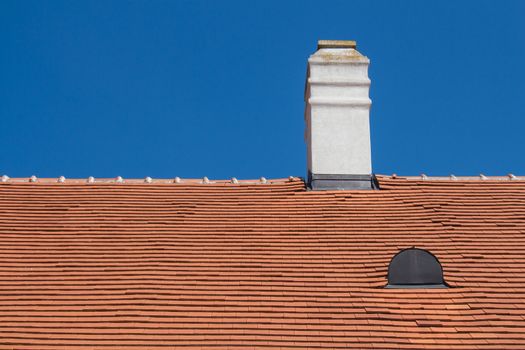 Old renewed orange roof with a white chimney and a roof window. Bright summer blue sky in the background.