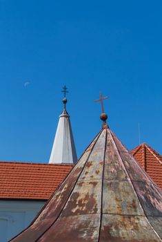 Older and new parts of the roofs of the church of Saint Peter and Paul in Cifer, Slovakia. Two crosses on the top of the towers. Blue sky with moon.