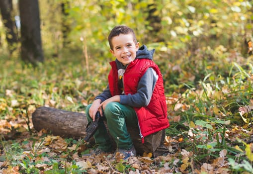 Joyfull boy sitting on log in autumn forest
