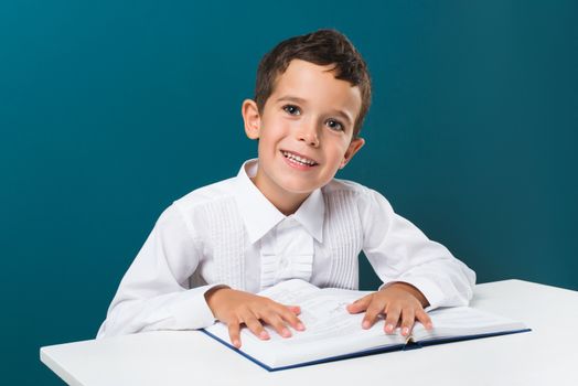 Smiling boy with book on the table, blue background