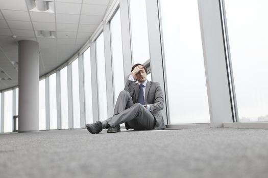 Businessman sitting on floor in office near window