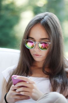 Beautiful young girl with smartphone sitting outdoors