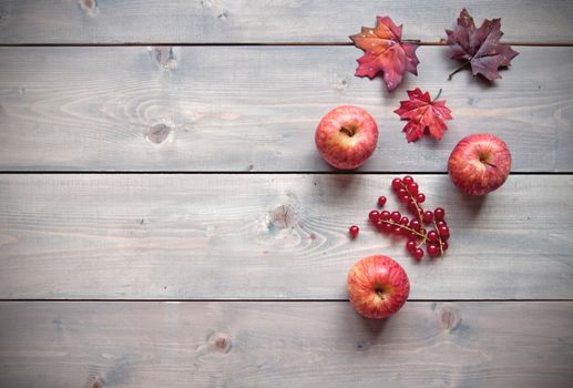 Red apples over a wooden background with maple leaves 