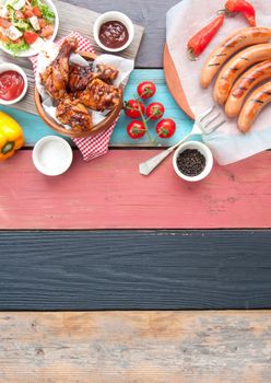 Selection of grilled barbecue meat including chicken and sausages with salad on top of a wooden table