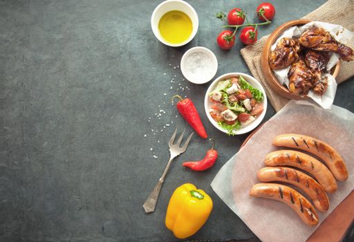 Selection of grilled chicken and sausages with salad on top of a wooden table