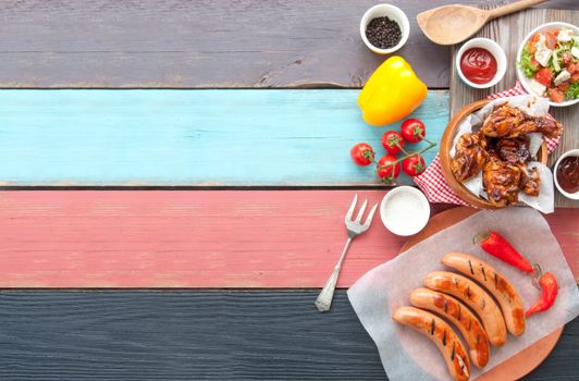 Selection of grilled barbecue meat including chicken and sausages with salad on top of a wooden table