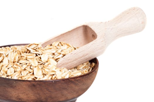 Wooden bowl with oats flakes pile on white background.