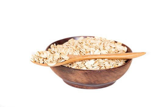 Wooden bowl with oats flakes pile on white background.